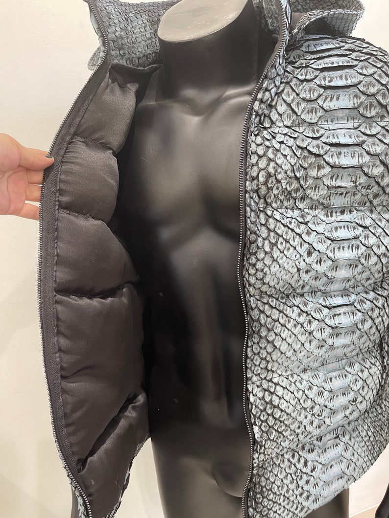 May include: A blue snakeskin jacket with a zipper closure and a black quilted lining. The jacket is unzipped to show the lining.