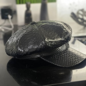 May include: A black leather newsboy cap with a snakeskin pattern.