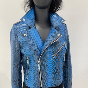 以下が含まれることがあります： シルバーのジッパーとスナップが付いた、青いヘビ革模様のレザージャケット。ノッチカラーと複数のポケットを備えた、クラシックなバイカースタイルです。色は鮮やかな青と黒のミックスで、質感のある外観を作り出しています。