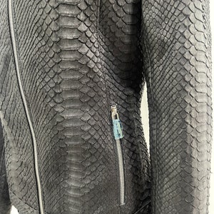 May include: A black leather jacket with a snakeskin pattern. The jacket has a zip closure and two zipped pockets.