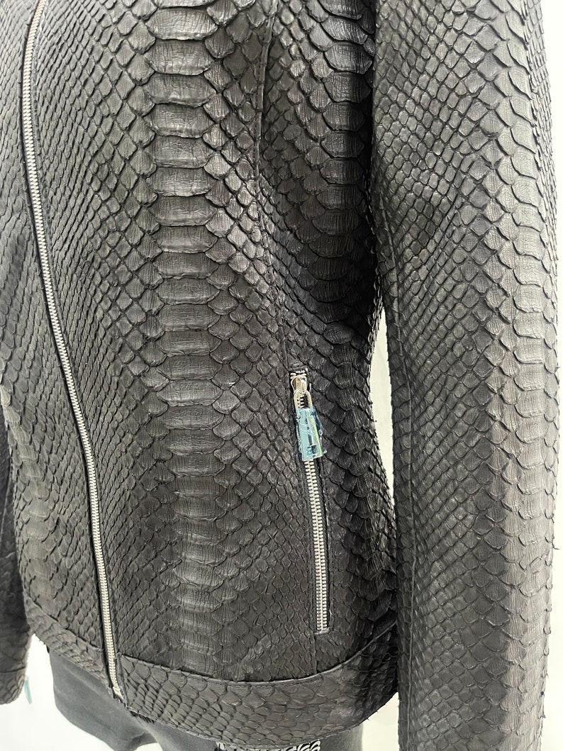 May include: A black leather jacket with a snakeskin pattern. The jacket has a zip closure and two zipped pockets.