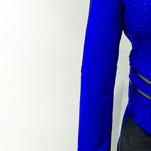 K&ouml;nnte beinhalten: Eine blaue Schlangenlederjacke mit Rei&szlig;verschluss. Die Jacke befindet sich an einem Mannequin und der &Auml;rmel ist hochgekrempelt.