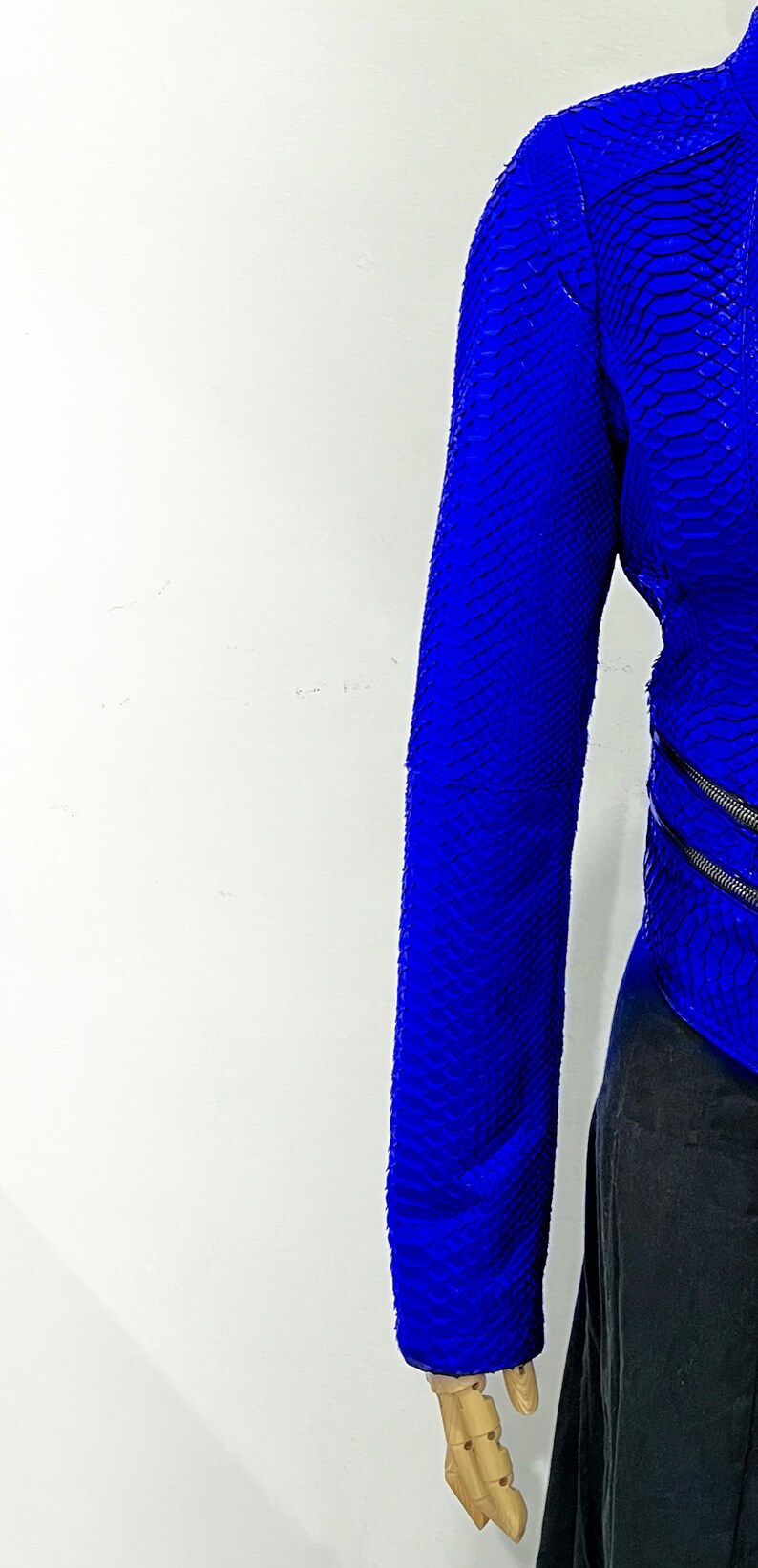 K&ouml;nnte beinhalten: Eine blaue Schlangenlederjacke mit Rei&szlig;verschluss. Die Jacke befindet sich an einem Mannequin und der &Auml;rmel ist hochgekrempelt.