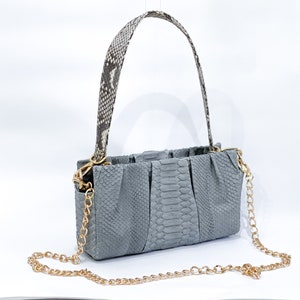 May include: A gray snakeskin handbag with a gold chain strap and a snakeskin top handle.