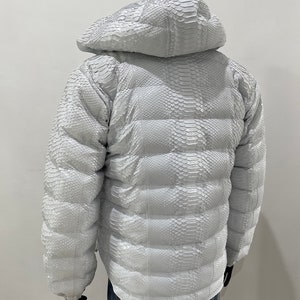 May include: White puffer jacket made of snakeskin with a hood. The jacket has a quilted design and is fully lined.