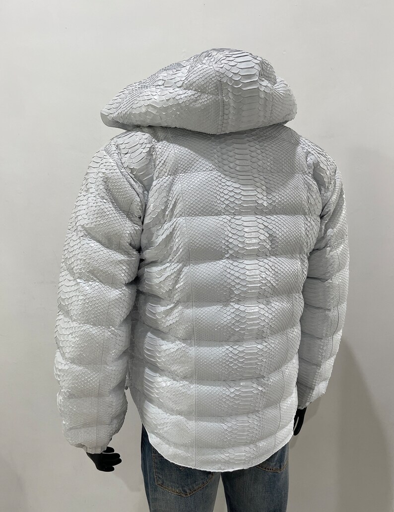 May include: White puffer jacket made of snakeskin with a hood. The jacket has a quilted design and is fully lined.