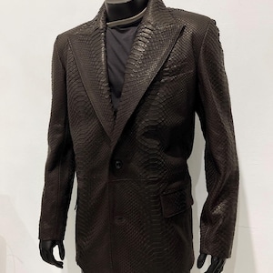 以下が含まれることがあります： シングルボタン留めのブラウンのスネークスキンブレザー。ブレザーはノッチドラペルと左側にポケットが付いています。