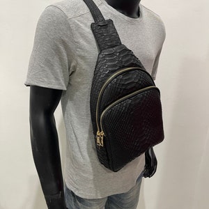 May include: A black leather crossbody bag with a snakeskin pattern and gold-toned hardware. The bag has two zippered compartments and a strap that can be adjusted to fit comfortably on the shoulder.