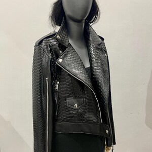 May include: A black leather jacket with a snakeskin pattern. The jacket has a zipper closure, two pockets, and a collar. The jacket is worn by a mannequin with a black beret.