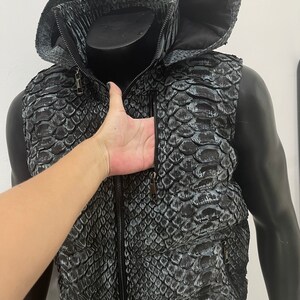 May include: A black and grey snakeskin vest with a zip fastening and a hood. The vest has two pockets on the front.