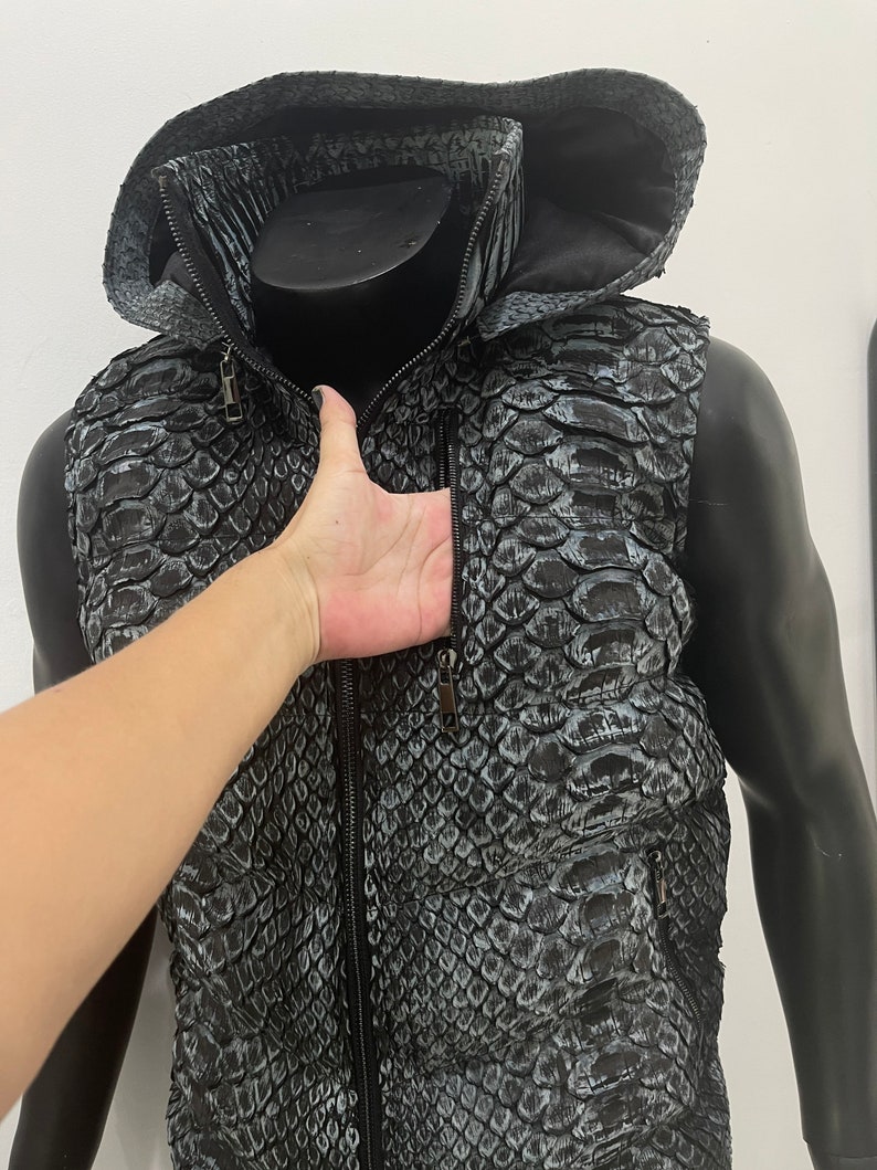 May include: A black and grey snakeskin vest with a zip fastening and a hood. The vest has two pockets on the front.