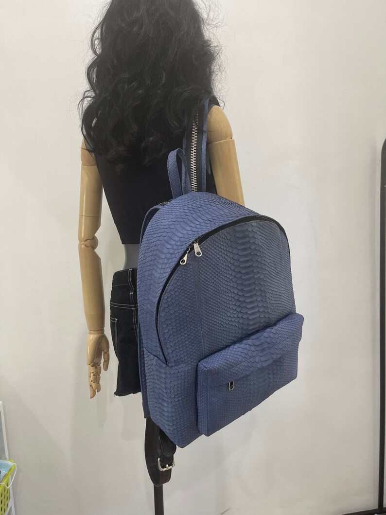 K&ouml;nnte beinhalten: Ein blauer Rucksack aus Schlangenleder mit einer Fronttasche und silbernen Beschl&auml;gen.