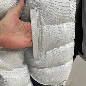 May include: White puffer jacket made of snakeskin with a zip fastening and a pocket on the side.