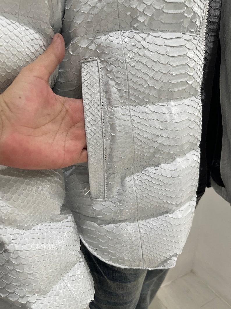 May include: White puffer jacket made of snakeskin with a zip fastening and a pocket on the side.