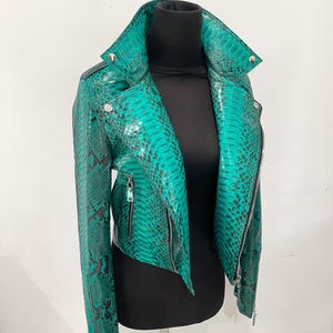 May include: A green snakeskin leather jacket with a zipper closure. The jacket has a stand-up collar and long sleeves.