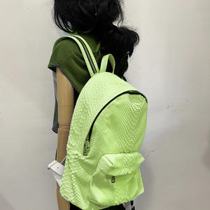 May include: A bright green snakeskin backpack with a zipper closure. The backpack is being worn by a mannequin with black hair and a black beret.