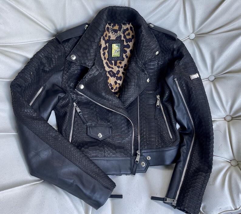 Może przedstawiać: Czarna sk&oacute;rzana kurtka motocyklowa z wzorem sk&oacute;ry węża i detalami z zamkiem błyskawicznym. Kurtka ma skr&oacute;coną długość i kołnierz.