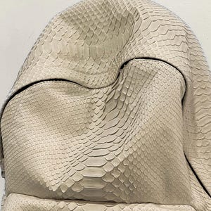 Op de afbeelding: Een close-up van een lichtbeige schlangenleren handtas met een textuur.