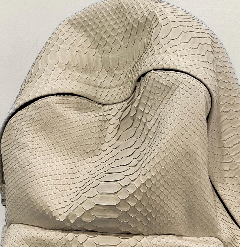 Op de afbeelding: Een close-up van een lichtbeige schlangenleren handtas met een textuur.