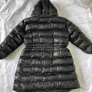 May include: Black puffer coat with a hood, featuring a snakeskin pattern. The coat has a cinched waist and a quilted design. The back view shows the full length of the coat, which is on a white background.