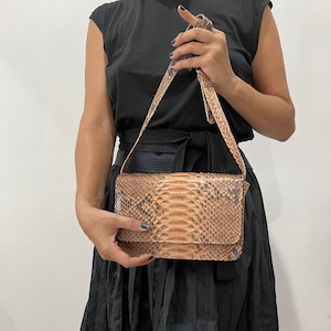 May include: A brown snakeskin crossbody bag with a black strap and a black belt around the waist.