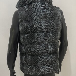 May include: A black sleeveless puffer vest with a snakeskin pattern. The vest has a hood and a zip closure.