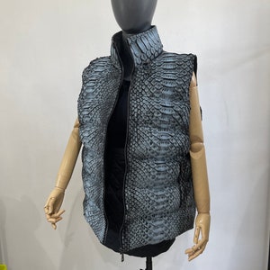May include: A sleeveless puffer vest with a zip closure. The vest is made of a grey snakeskin-patterned fabric.