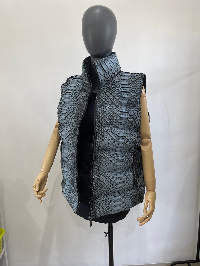 May include: A sleeveless puffer vest with a zip closure. The vest is made of a grey snakeskin-patterned fabric.