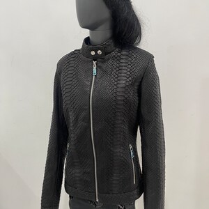 May include: Black leather jacket with a snakeskin pattern and a zip closure. The jacket has a stand-up collar and long sleeves.