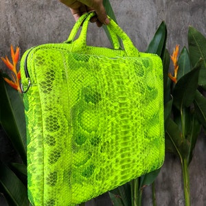 May include: A bright neon green snakeskin laptop bag with a top handle. The bag is made of real snakeskin and has a unique, textured pattern.