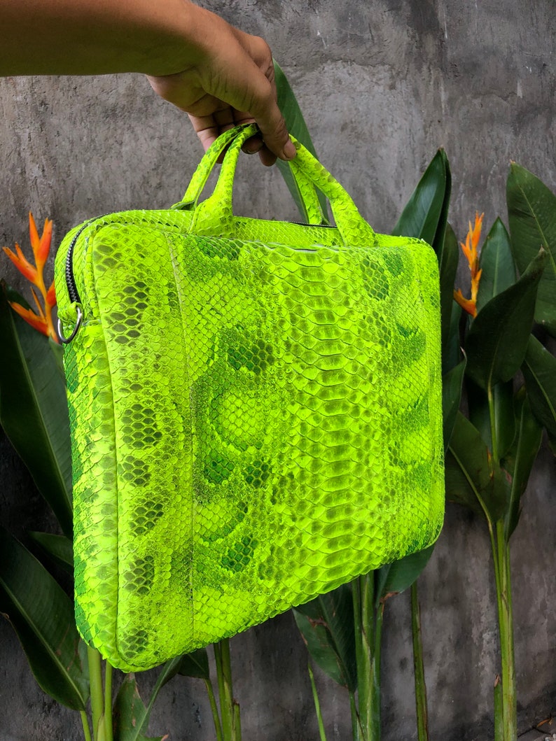 May include: A bright neon green snakeskin laptop bag with a top handle. The bag is made of real snakeskin and has a unique, textured pattern.