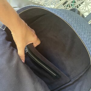 K&ouml;nnte beinhalten: Ein blauer Lederrucksack mit einer Rei&szlig;verschlusstasche auf der Vorderseite. Der Rucksack ist offen und das Innere ist mit einem dunklen Stoff ausgekleidet.