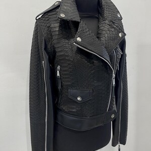 Może przedstawiać: Czarna sk&oacute;rzana kurtka motocyklowa z wzorem sk&oacute;ry węża. Kurtka ma zamek błyskawiczny, dwie kieszenie i pasek w talii.