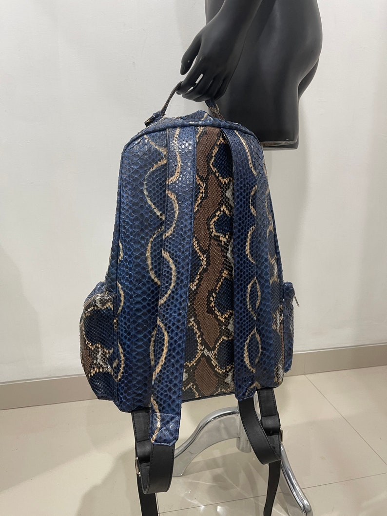 Op de afbeelding: Een blauwe en bruine slangleren rugzak met verstelbare banden. De rugzak heeft een ritsvak aan de voorkant en een ritsvak aan elke zijde.