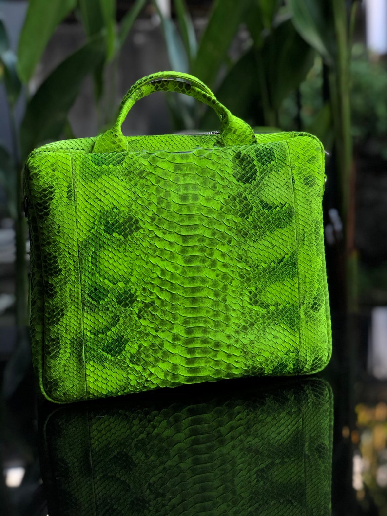 May include: A bright green snakeskin leather briefcase with a top handle and a zip closure.