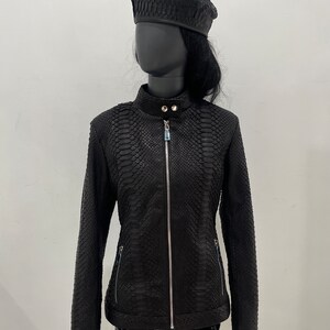 May include: A black leather jacket with a snakeskin pattern. The jacket has a zip fastening and two pockets on the sides. The jacket is being modelled on a mannequin wearing a black beret.