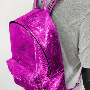 May include: A bright pink snakeskin backpack with a zipper closure. The backpack has a shiny, metallic finish.