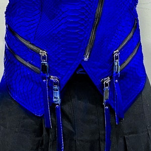 K&ouml;nnte beinhalten: Eine blaue Lederjacke mit Rei&szlig;verschluss und mehreren Rei&szlig;verschlussdetails. Die Jacke hat ein Schlangenhautmuster.