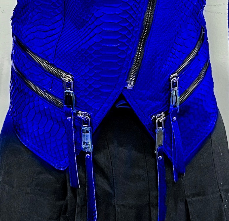 K&ouml;nnte beinhalten: Eine blaue Lederjacke mit Rei&szlig;verschluss und mehreren Rei&szlig;verschlussdetails. Die Jacke hat ein Schlangenhautmuster.