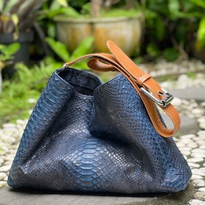 以下が含まれることがあります： 青いヘビ革のハンドバッグで、茶色の革のストラップとバックルが付いています。