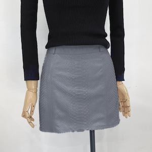 Peut inclure: Une mini-jupe grise à motif peau de serpent.