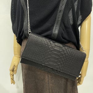 May include: A black snakeskin clutch bag with a silver chain strap. The bag has a flap closure and a textured snakeskin pattern.