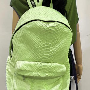 May include: A bright green snakeskin backpack with a zipper closure and a small pocket on the front. The backpack has a white strap.