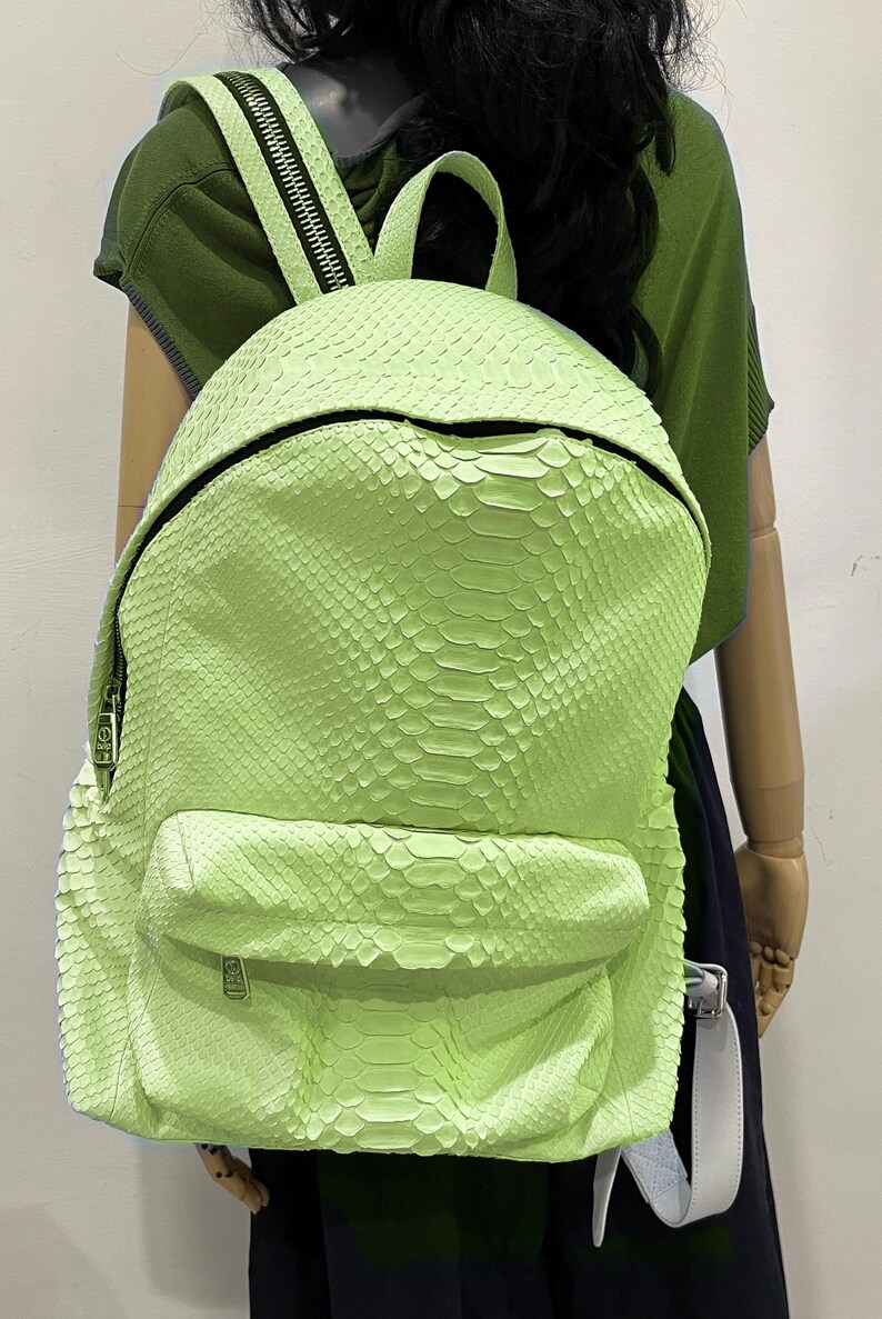 May include: A bright green snakeskin backpack with a zipper closure and a small pocket on the front. The backpack has a white strap.
