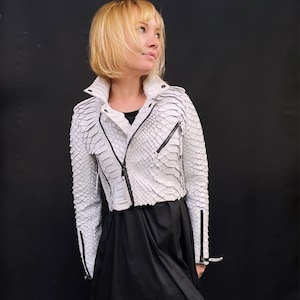May include: A white leather jacket with a snake skin pattern. The jacket has a zip fastening and black trim.