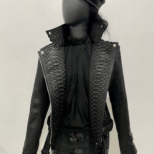 May include: A black leather jacket with a snakeskin pattern. The jacket has a zip fastening and a belt at the waist. The jacket is worn over a black top and black shorts with sequins.