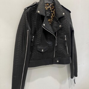 Może przedstawiać: Czarna sk&oacute;rzana kurtka ze wzorem sk&oacute;ry węża i podszewką w panterkę. Kurtka ma zamek błyskawiczny i dwie kieszenie.