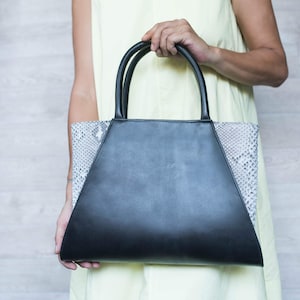 May include: A black leather handbag with a grey snakeskin pattern on the sides. The bag has two top handles.