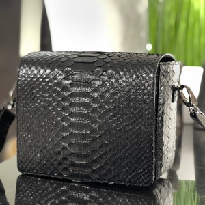 May include: A black snakeskin crossbody bag with a flap closure and a silver chain strap.
