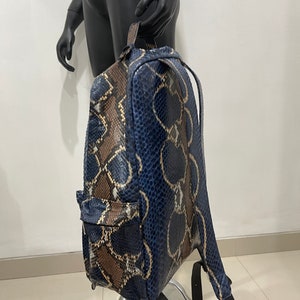 Op de afbeelding: Een blauwe en bruine slangleren rugzak met verstelbare banden. De rugzak heeft een ritsvak aan de voorkant.